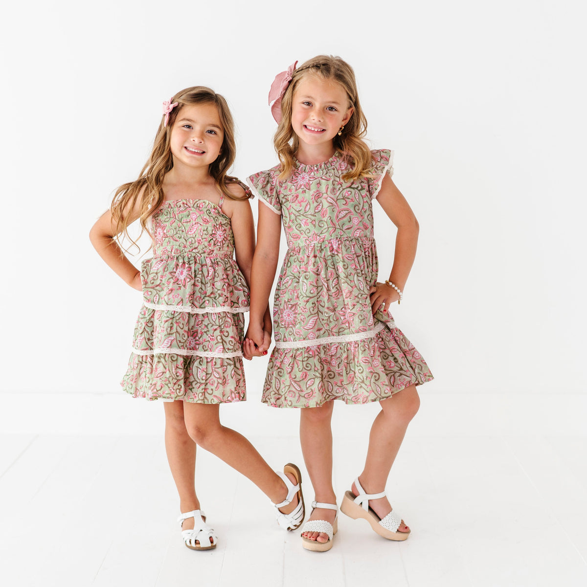 Two young girls wearing matching floral dresses on a white background