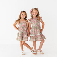 Two young girls wearing matching floral dresses on a white background