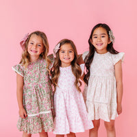 Three young girls wearing floral dresses against a pink background