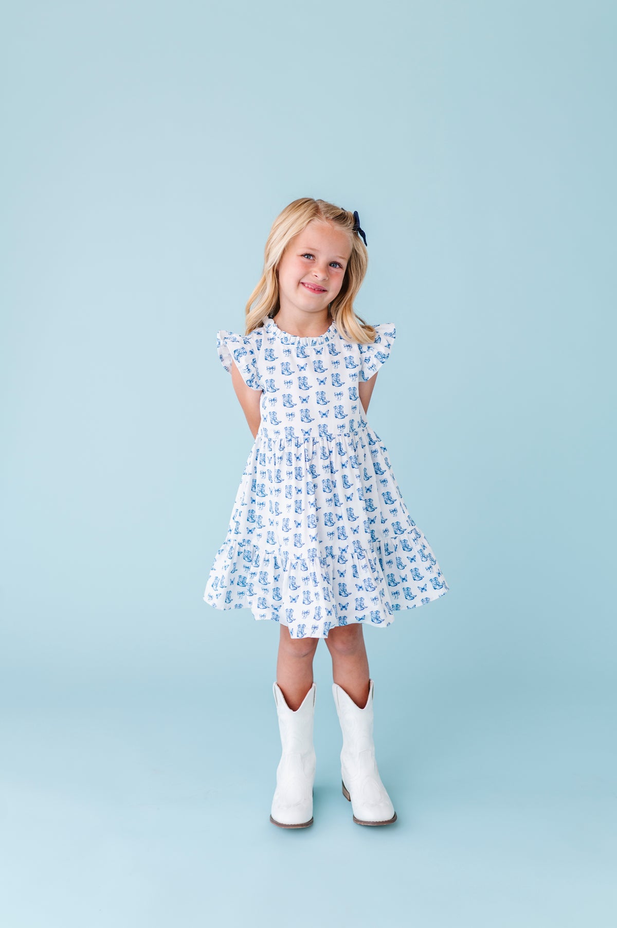 Young girl wearing al dress in a butterflies and boots print and white boots against a light blue background