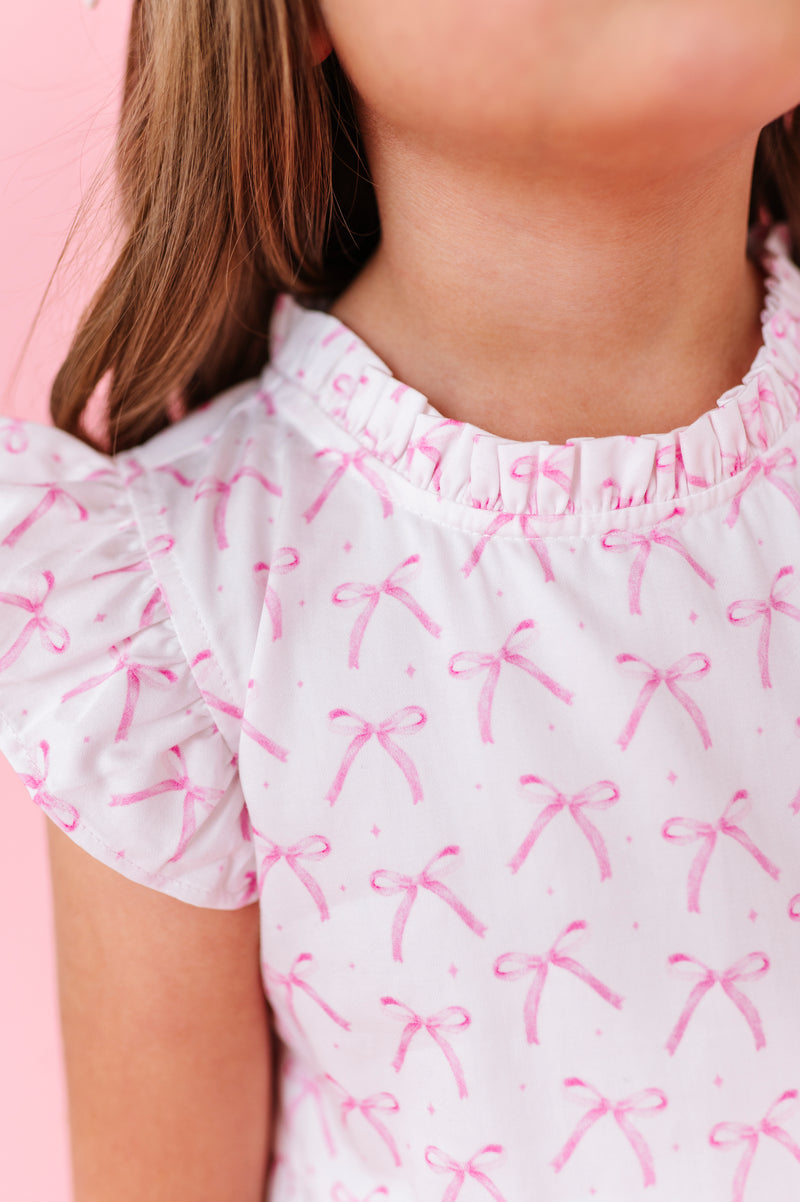 Close-up of a person wearing a white dress with pink bow patterns against a pink background.