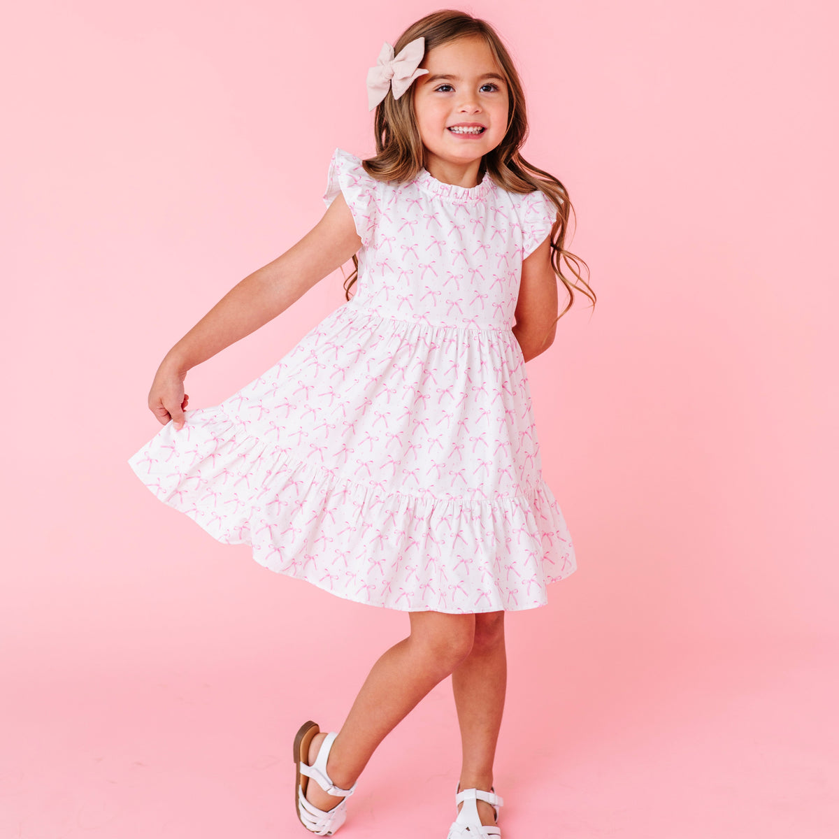 Young girl wearing a white dress with pink bows against a pink background