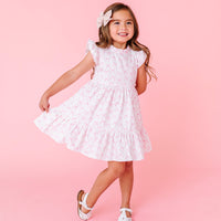 Young girl wearing a white dress with pink bows against a pink background