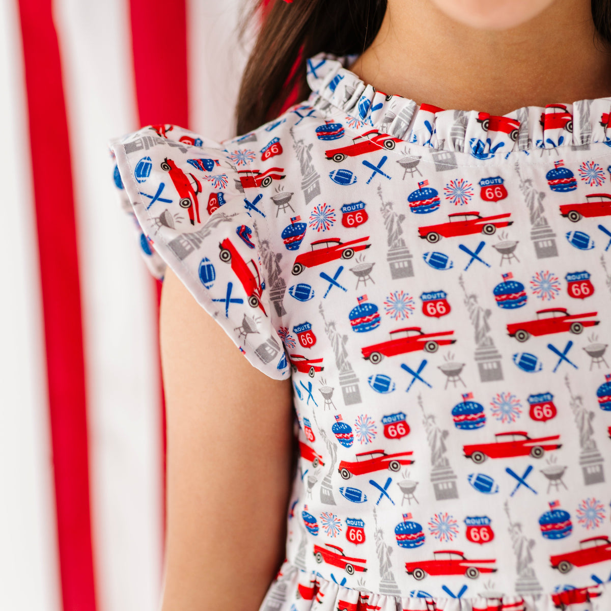 Young girl in a red, white, and blue Americana print dress standing in front of an American flag.