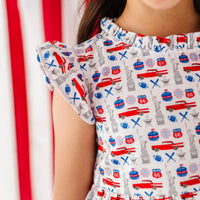 Young girl in a red, white, and blue Americana print dress standing in front of an American flag.