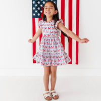 Young girl in a red, white, and blue Americana print dress standing in front of an American flag.