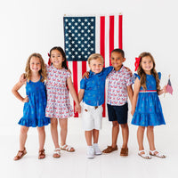Five children in patriotic outfits standing in front of an American flag on a white background