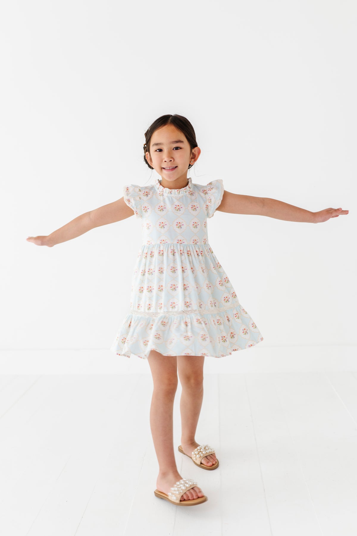 Young girl wearing a white dress with a floral pattern on a white background
