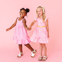 Two young girls wearing pink popsicle dresses standing against a pink background
