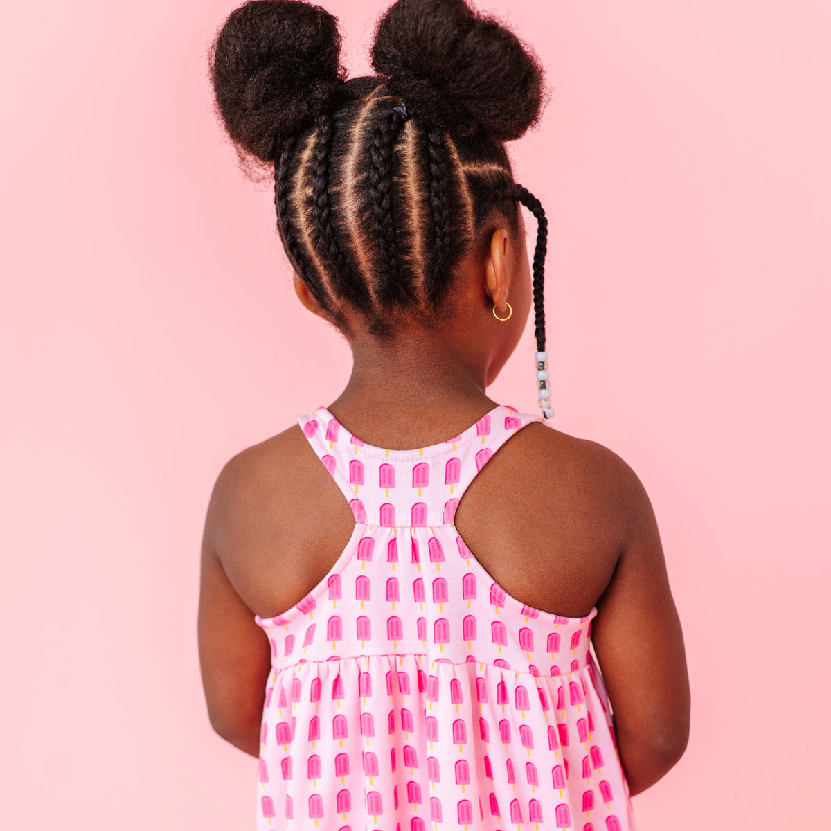Young girl in a pink popsicle dress standing against a pink background