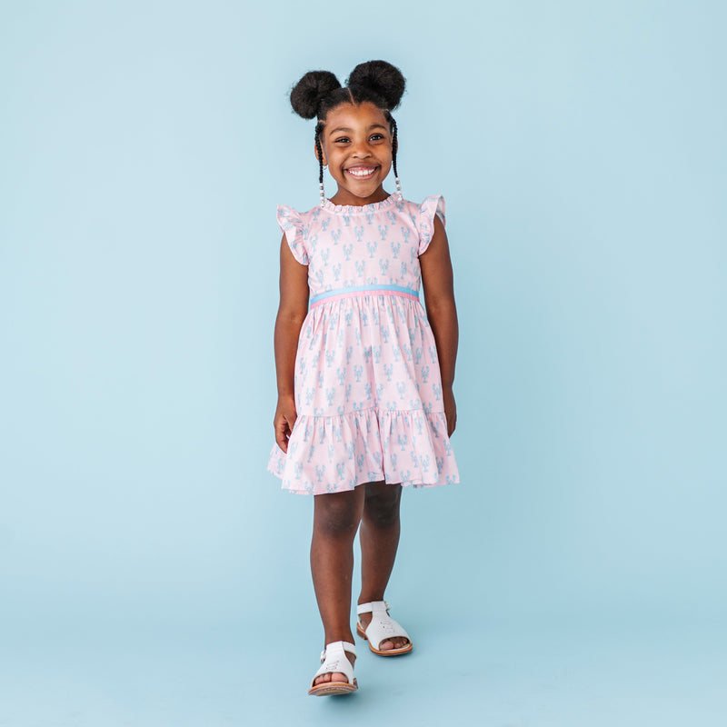 Young girl wearing a pink lobster print dress with a white background