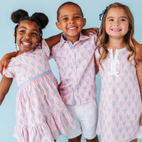 Three children wearing matching pink outfits with a blue background