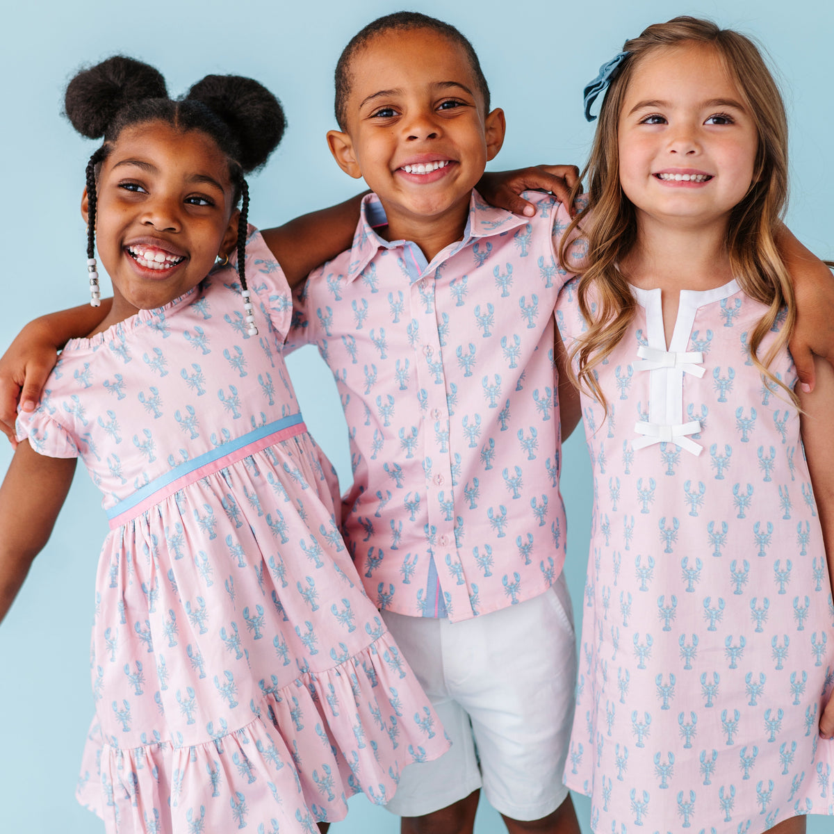 Three children wearing matching pink lobster outfits with a blue background