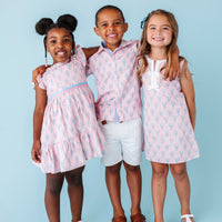 Three children wearing matching pink lobster outfits against a light blue background