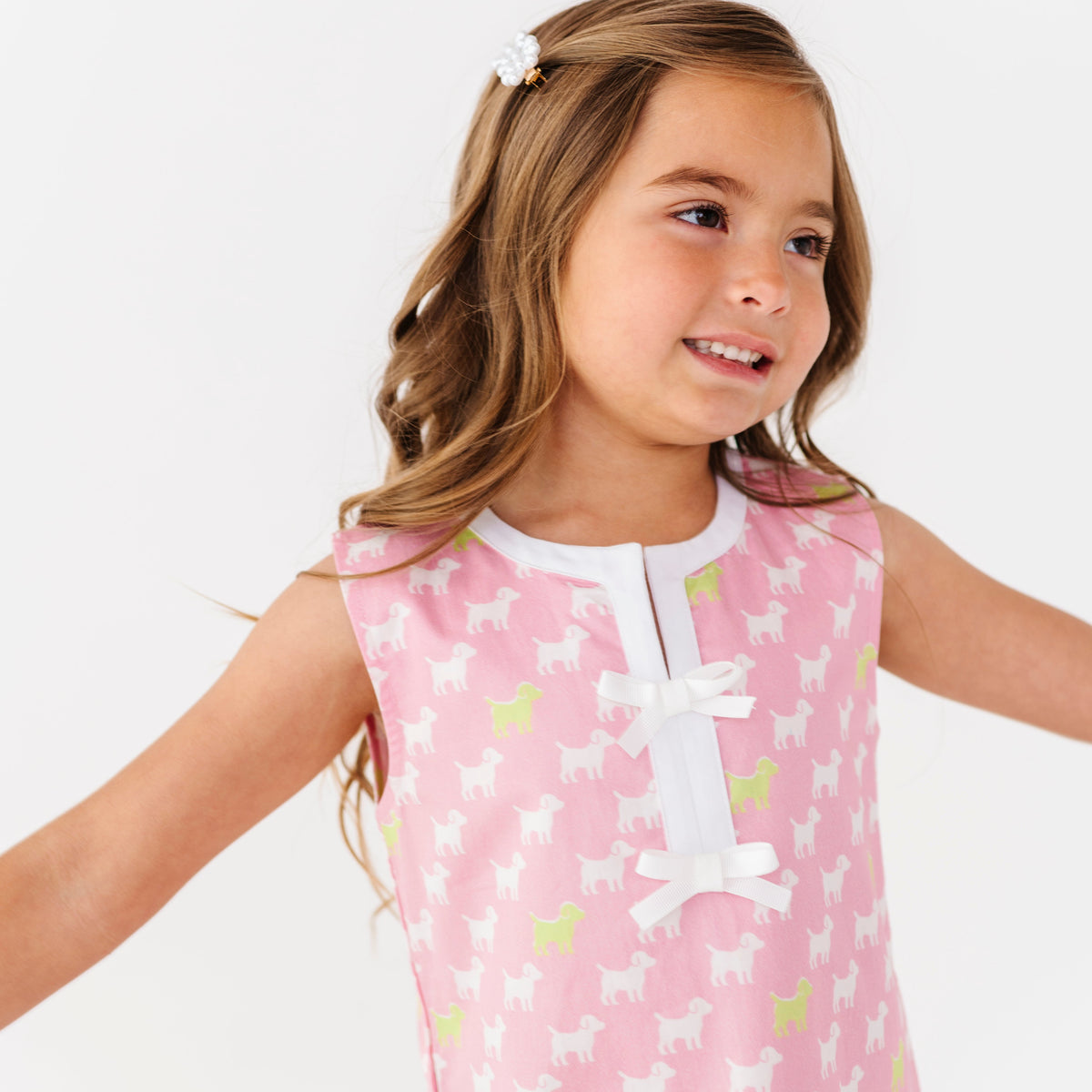 Young girl wearing a pink dress with white puppies on a white background
