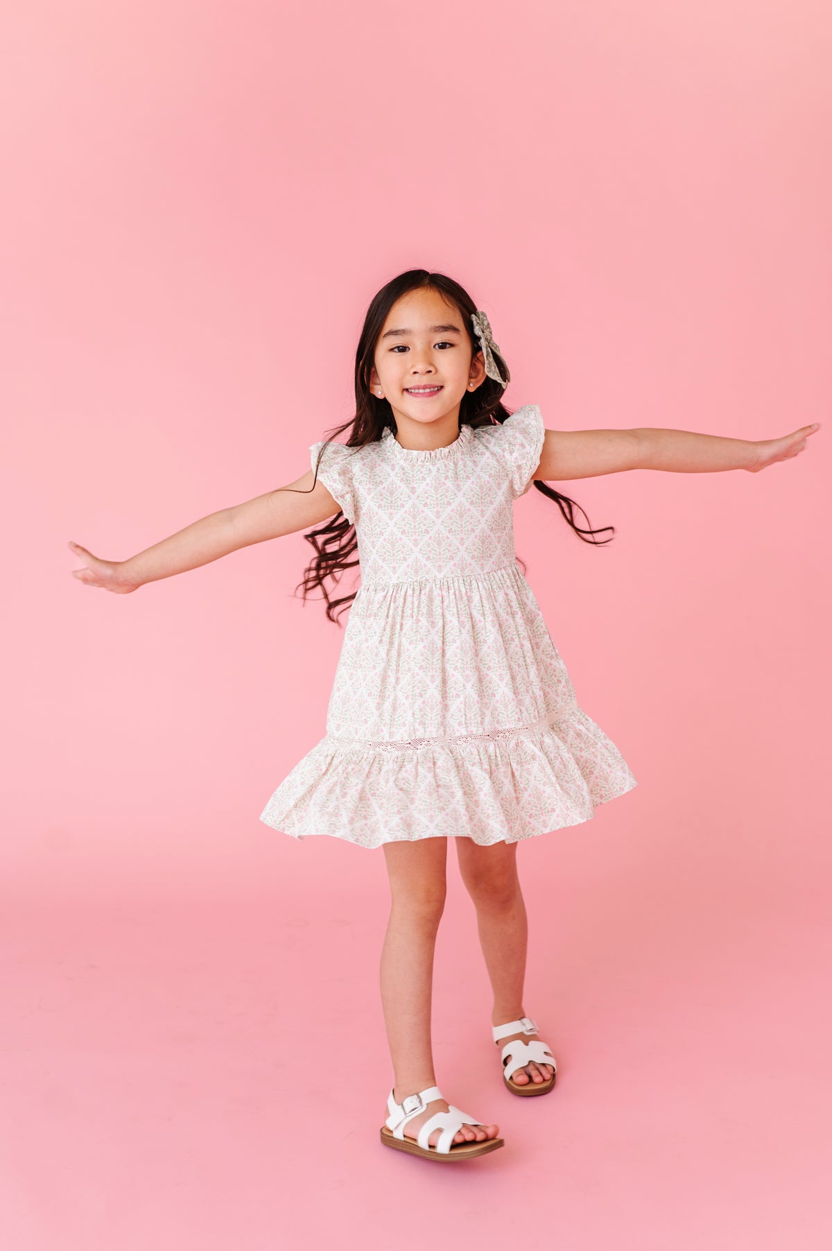 Young girl in a white lace dress standing against a pink background
